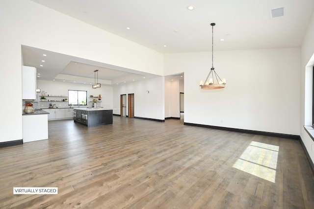 unfurnished living room featuring a notable chandelier, a raised ceiling, and dark wood-type flooring