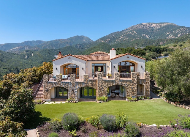 rear view of property with a balcony, a mountain view, and a yard