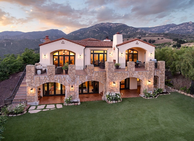 back house at dusk with a balcony, a mountain view, and a yard