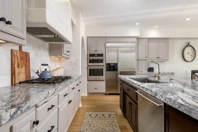 kitchen featuring sink, light hardwood / wood-style flooring, backsplash, custom exhaust hood, and appliances with stainless steel finishes