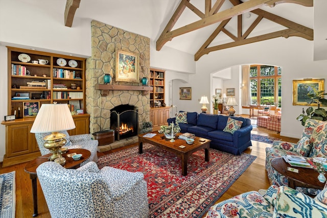 living room with beam ceiling, built in features, a stone fireplace, wood-type flooring, and high vaulted ceiling