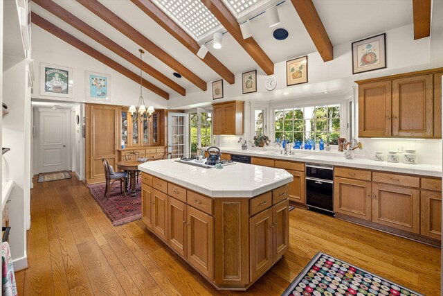 kitchen featuring beam ceiling, stainless steel gas stovetop, a kitchen island, light hardwood / wood-style floors, and decorative light fixtures