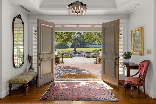 foyer featuring crown molding, hardwood / wood-style flooring, a raised ceiling, and a notable chandelier