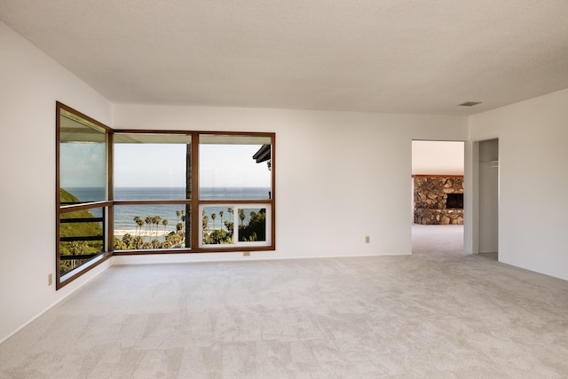 carpeted spare room with a fireplace, a textured ceiling, and a water view