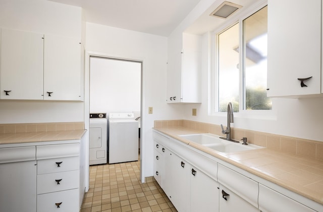 kitchen with tile counters, washer and clothes dryer, sink, and white cabinets