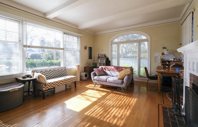 living area with beam ceiling, plenty of natural light, a tiled fireplace, and wood finished floors