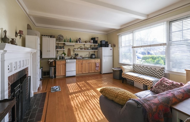 living room featuring beam ceiling, a tiled fireplace, and wood finished floors