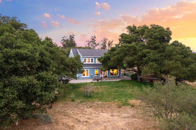 back house at dusk with a lawn and a patio