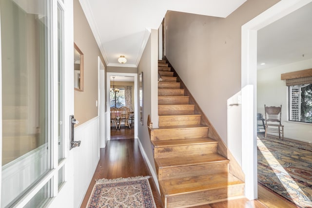 stairs featuring hardwood / wood-style floors, crown molding, and a notable chandelier