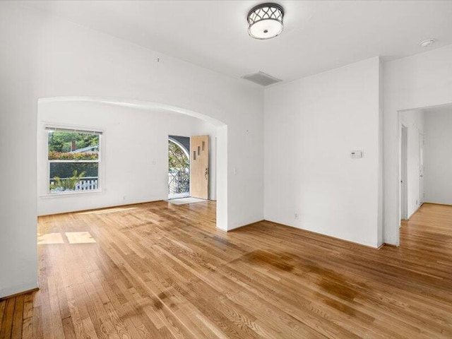 unfurnished room featuring arched walkways and light wood-style flooring