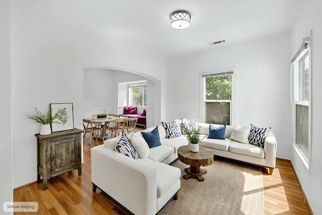 living room featuring arched walkways, wood finished floors, and visible vents