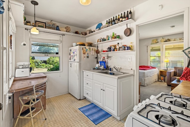 kitchen with white refrigerator, pendant lighting, sink, stove, and light tile patterned floors