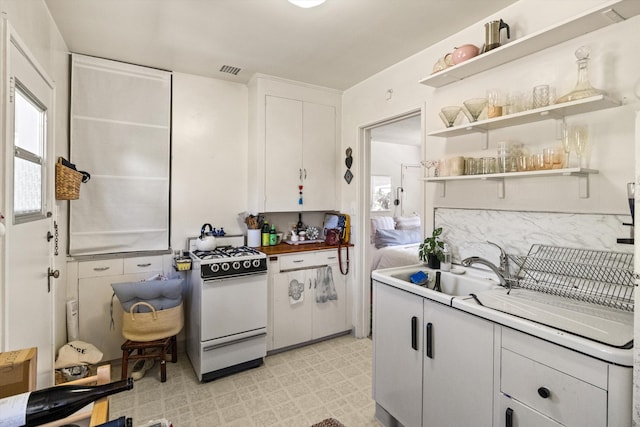 kitchen featuring white gas stove, white cabinetry, and light tile patterned flooring