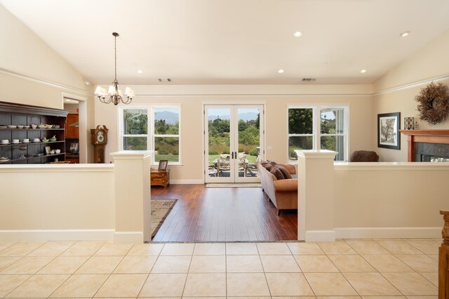 unfurnished living room with lofted ceiling, light hardwood / wood-style flooring, a chandelier, and french doors