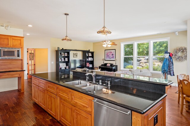 kitchen featuring appliances with stainless steel finishes, a center island with sink, sink, pendant lighting, and dark wood-type flooring