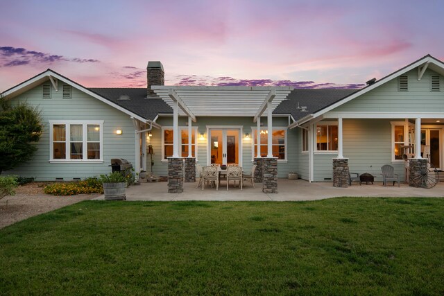 back house at dusk with a patio area and a lawn