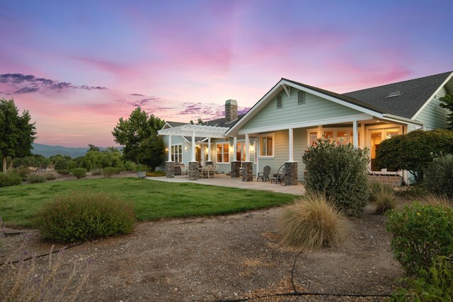 back house at dusk featuring a yard and a pergola