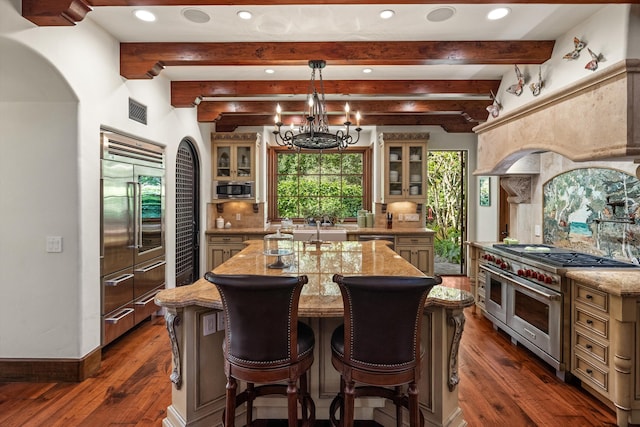 kitchen with built in appliances, decorative light fixtures, dark hardwood / wood-style floors, an island with sink, and a notable chandelier