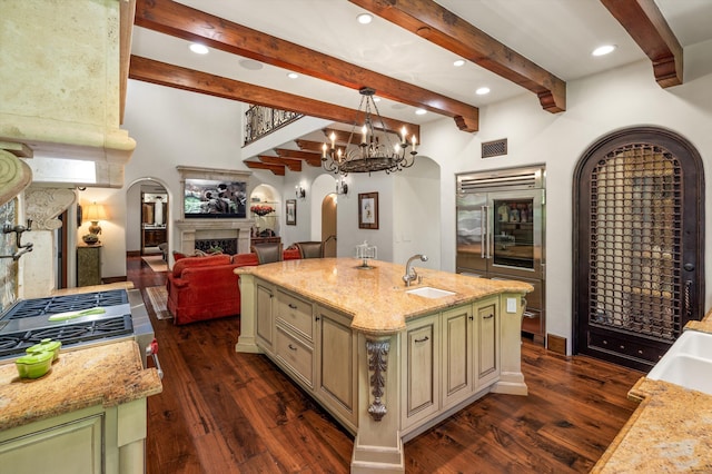 kitchen with light stone counters, hanging light fixtures, sink, and a center island with sink