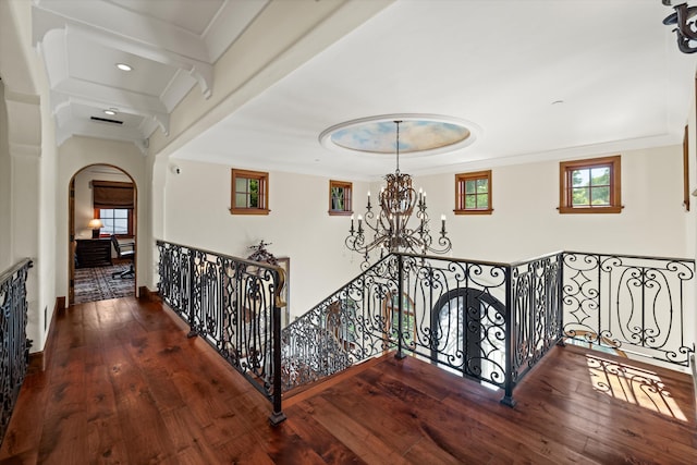 hall with a notable chandelier, hardwood / wood-style flooring, ornamental molding, and a raised ceiling