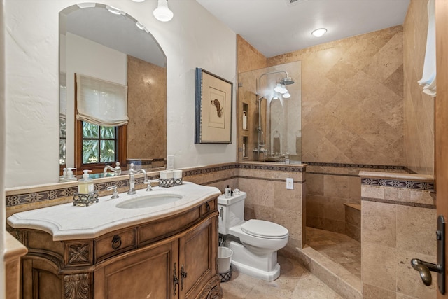 bathroom with toilet, tile walls, a tile shower, vanity, and tile patterned flooring