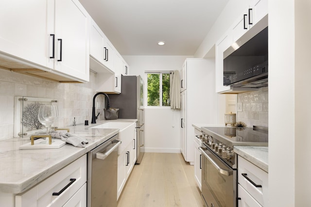 kitchen with light stone countertops, appliances with stainless steel finishes, white cabinets, and light hardwood / wood-style flooring