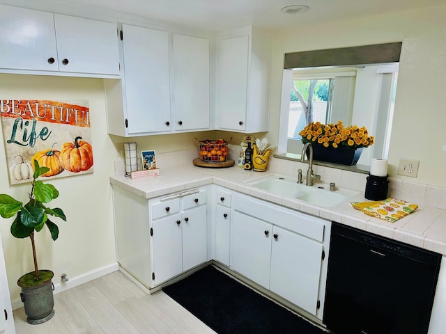 kitchen featuring black dishwasher, tile countertops, light wood finished floors, white cabinetry, and a sink