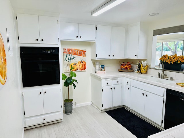 kitchen with black appliances, tile counters, white cabinets, and a sink