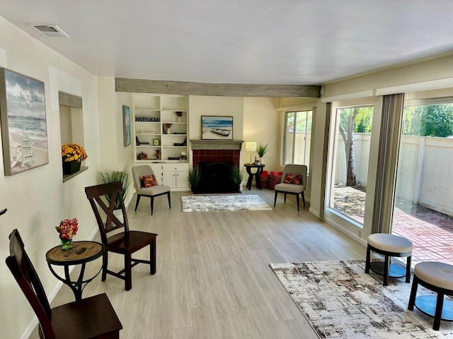 sitting room featuring light wood-style flooring, visible vents, built in features, baseboards, and a brick fireplace