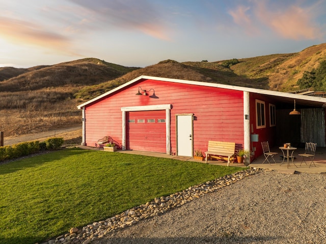 outdoor structure at dusk featuring an outbuilding, driveway, a mountain view, and a yard