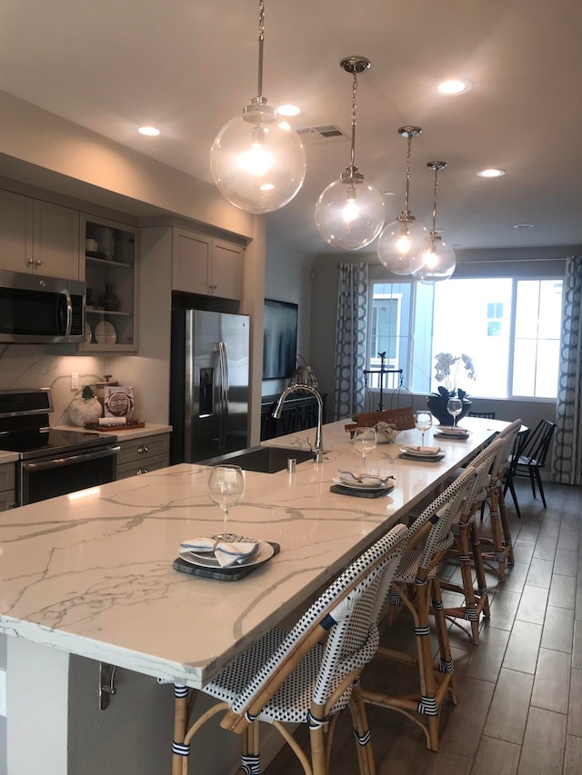 kitchen featuring a kitchen bar, hanging light fixtures, gray cabinetry, and appliances with stainless steel finishes