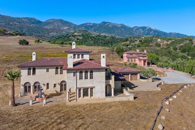 back of house with a chimney, a tiled roof, fence, a mountain view, and stucco siding