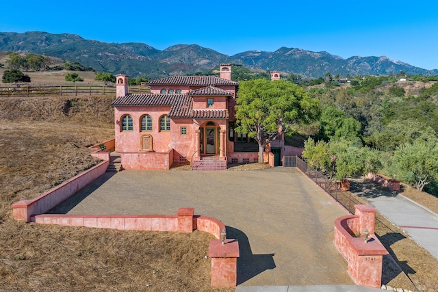 mediterranean / spanish-style home with a chimney, a tile roof, a mountain view, and fence