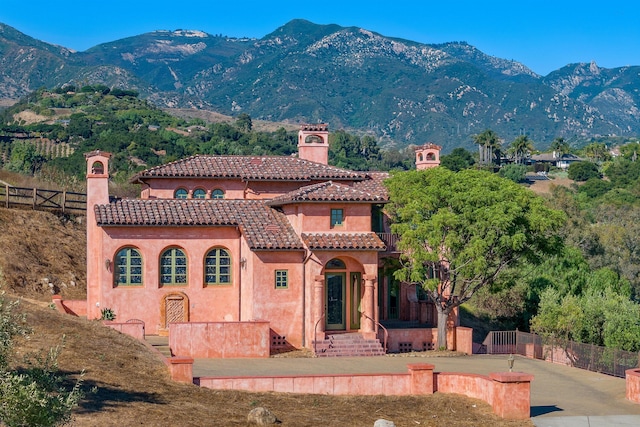 view of front of home with a chimney, fence, a mountain view, and a tiled roof