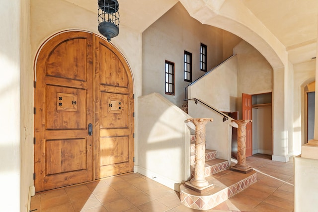 tiled entryway with a towering ceiling, baseboards, stairs, and arched walkways