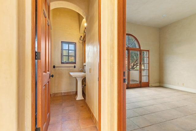 corridor with arched walkways, light tile patterned floors, and baseboards