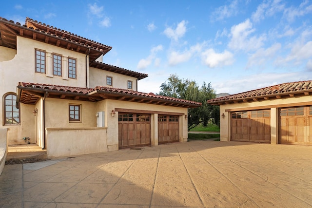 exterior space with a garage, driveway, a tile roof, and stucco siding