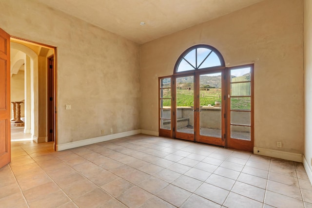 spare room with arched walkways, baseboards, and light tile patterned floors