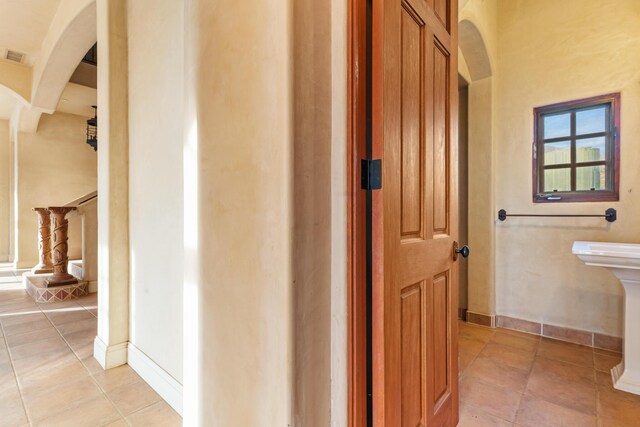 corridor with arched walkways, light tile patterned floors, stairs, and baseboards