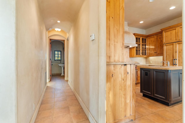 corridor featuring recessed lighting, baseboards, arched walkways, a sink, and light tile patterned flooring