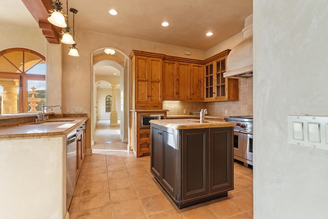 kitchen featuring arched walkways, decorative backsplash, custom range hood, appliances with stainless steel finishes, and a sink