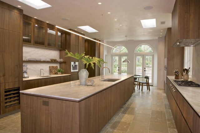 kitchen featuring a large island with sink, sink, stainless steel gas stovetop, and premium range hood