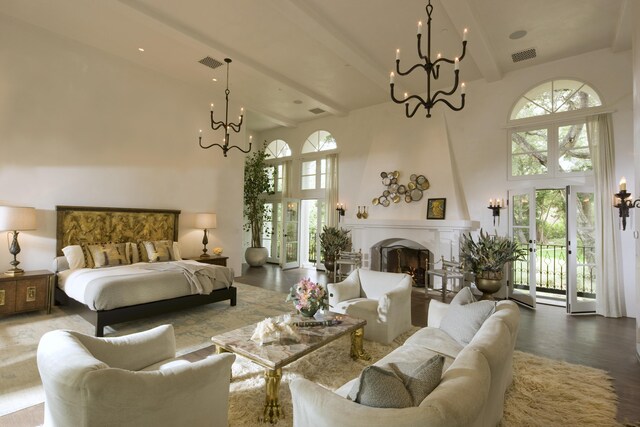 bedroom with hardwood / wood-style floors, a large fireplace, a towering ceiling, and a notable chandelier