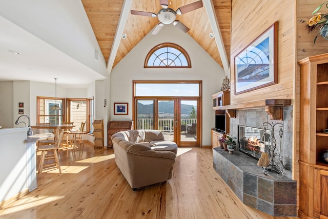 living room with a tiled fireplace, wood ceiling, high vaulted ceiling, ceiling fan, and light wood-type flooring