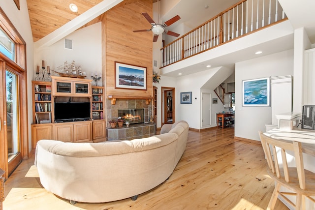 living room with light wood-type flooring, high vaulted ceiling, a tile fireplace, and ceiling fan