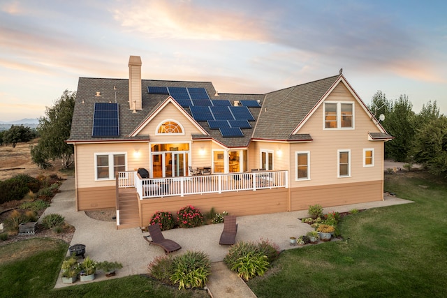 back house at dusk with a yard, a patio area, a deck, and solar panels