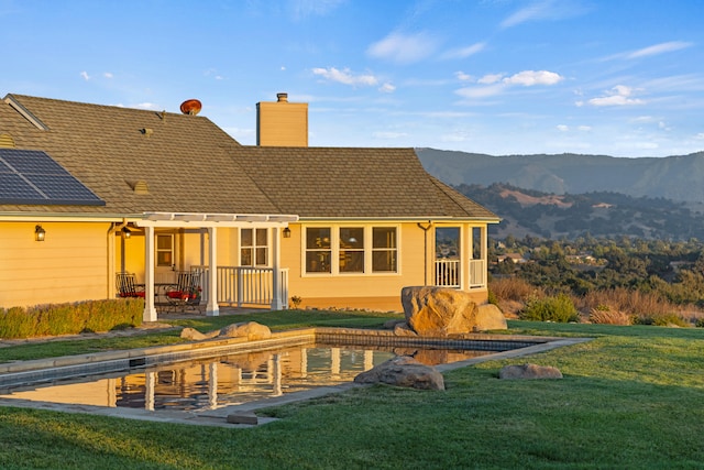 back of property with a pergola, a mountain view, and a lawn