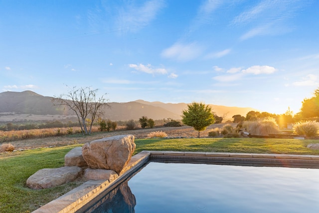 pool at dusk featuring a lawn, a rural view, and a mountain view