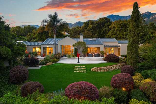 back house at dusk with a mountain view, solar panels, and a yard