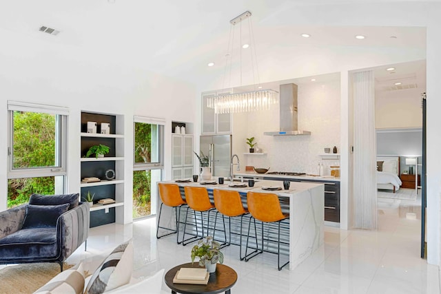 kitchen featuring a kitchen bar, wall chimney exhaust hood, a notable chandelier, an island with sink, and pendant lighting